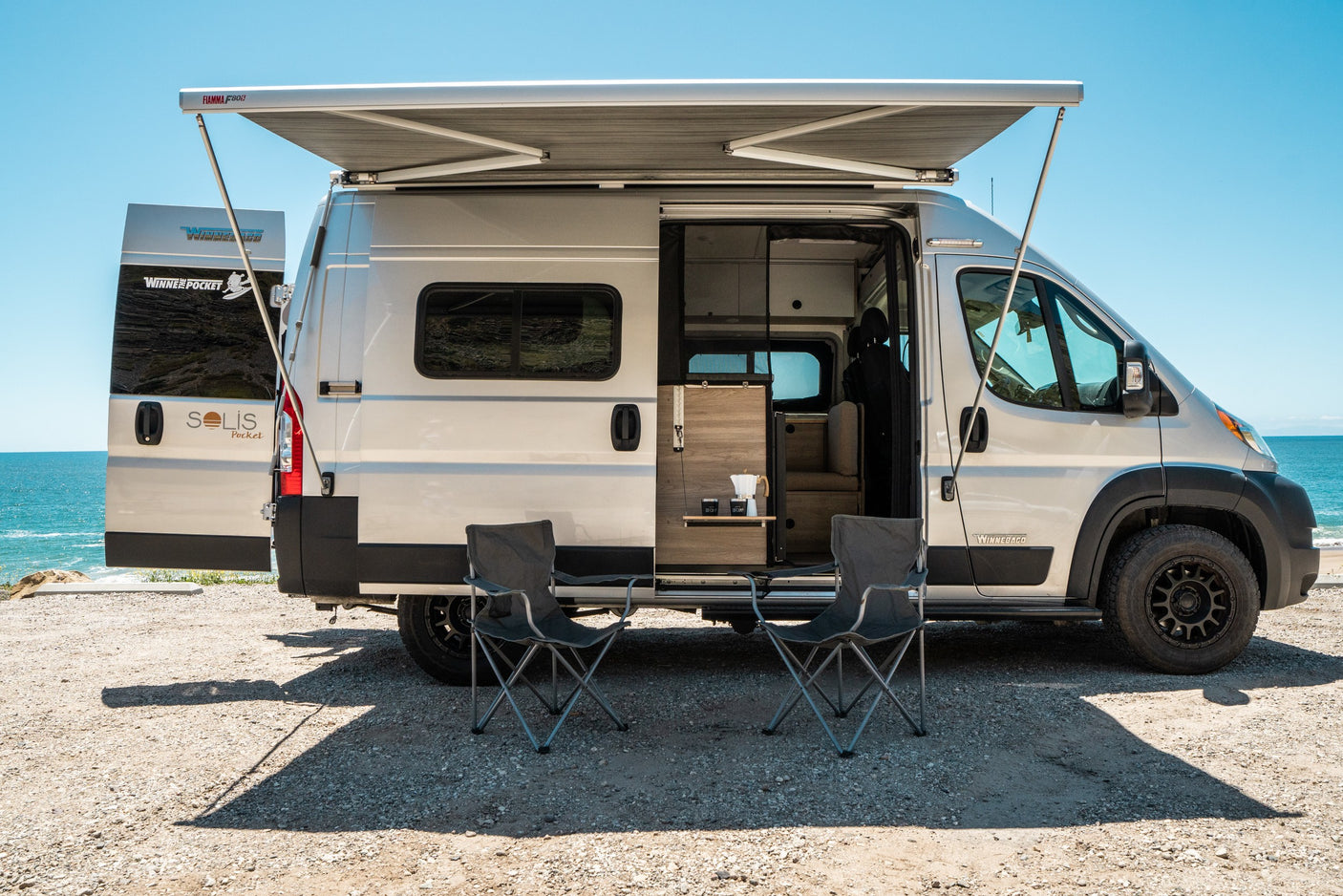 Enjoy this Winnebago Solis Pocket camper van for your next RV rental, featuring an awning & chairs by the ocean.