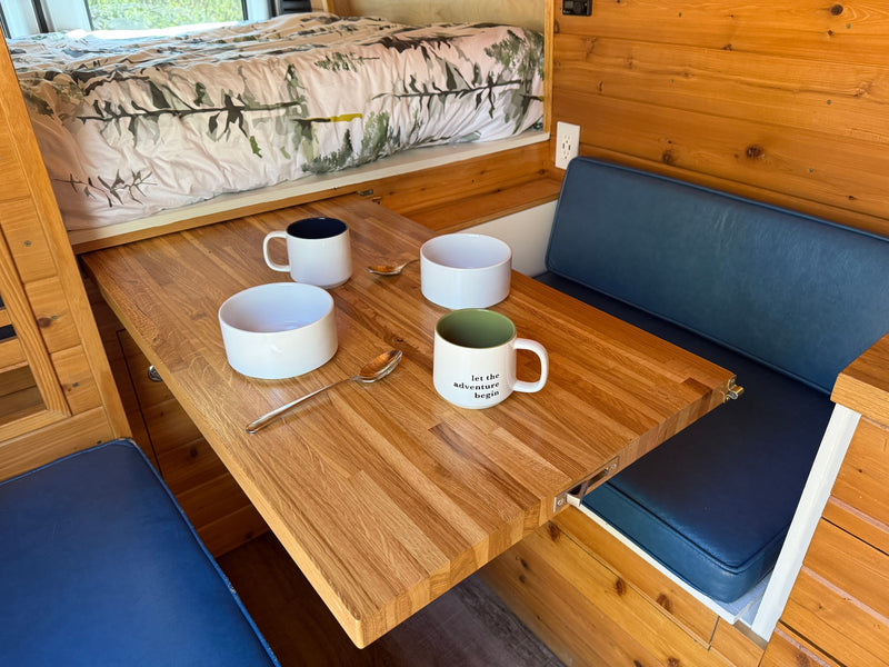 Step inside this inviting RV rental with a built-in wooden table, comfy blue cushions, and a cozy bed. Adventure awaits! — photo 7