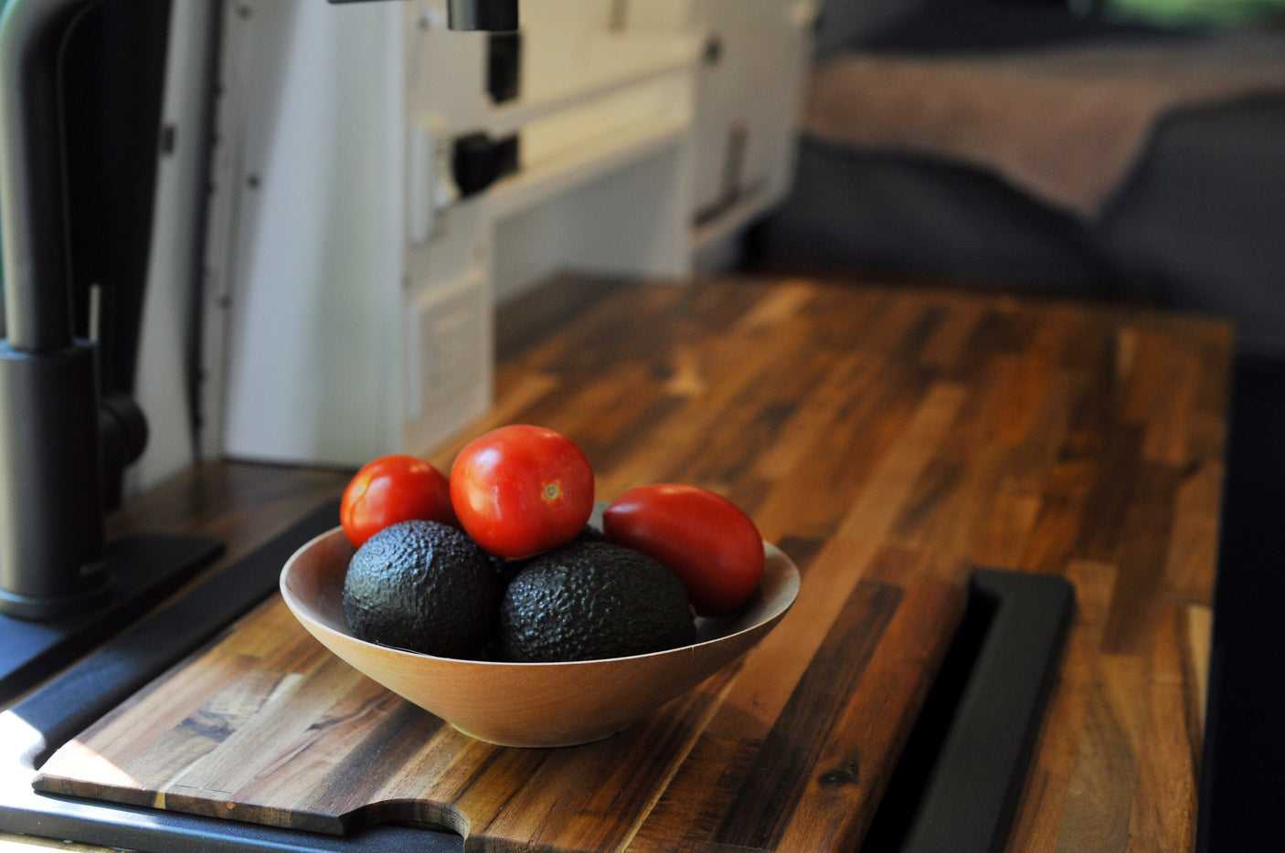 Bowl of fresh avocados and tomatoes on a wooden counter in an RV rental. Ideal for healthy travel meals.