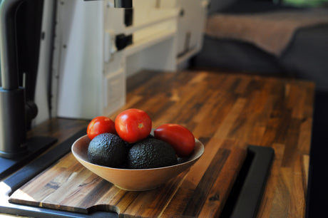 Bowl of fresh avocados and tomatoes on a wooden counter in an RV rental. Ideal for healthy travel meals.