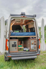 Explore this cozy RV rental's clever camper van interior, featuring a raised bed, organized storage, and utility panels for adventure.