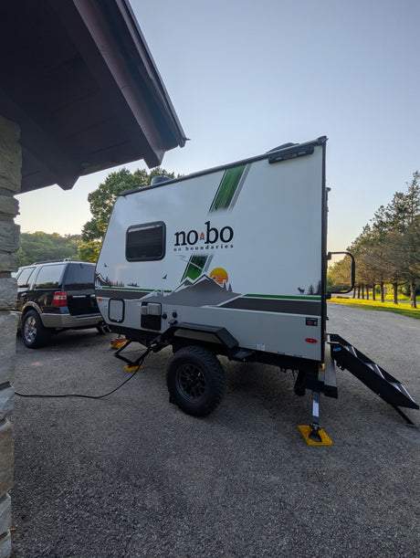 RV rental: A white "no bo" travel trailer, towed by an SUV on asphalt, shows connected power. Set for camping adventure.
