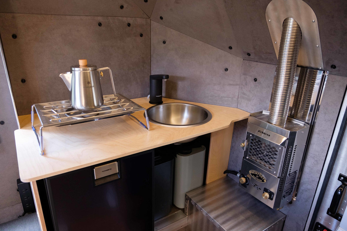Compact RV rental kitchenette: sink, Snow Peak kettle on stove, Dometic fridge, and Dickinson heater for comfort.