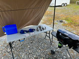 RV rental outdoor kitchen setup: portable grill, table, water jug & dishes under awning. Perfect for camping!