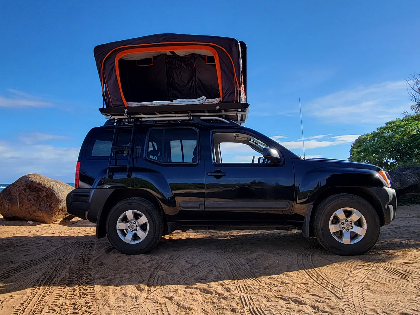 Black SUV with open rooftop tent on a sandy beach under blue sky, perfect for an RV rental adventure.