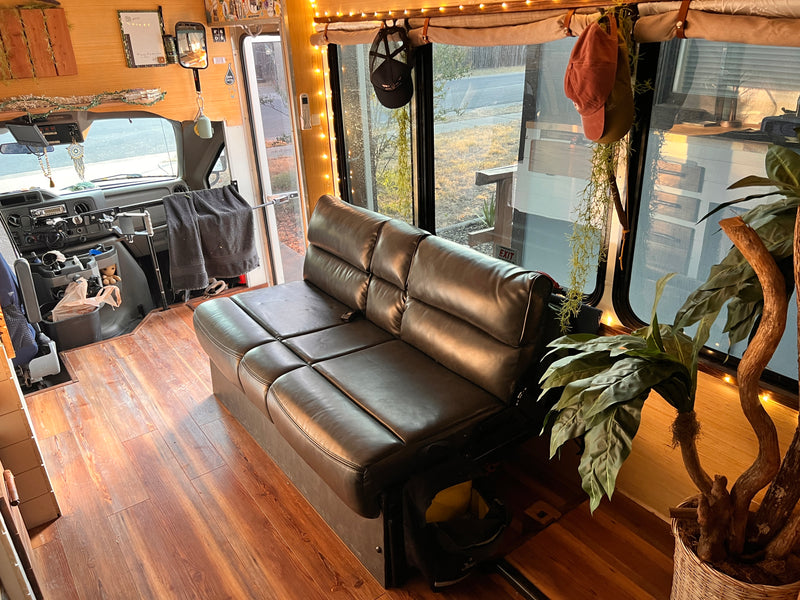 Cozy RV rental interior with a dark leather sofa & wood floors. Driver's area visible, ready for your next adventure. — photo 13