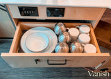 RV rental kitchen drawer open, revealing stacked plates, bowls, and metal cups. USB ports & power outlets above.