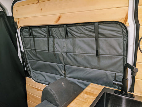 Cozy RV rental interior featuring wood walls, padded window insulation, kitchen sink with faucet, & comfy seating. Ideal for travel.
