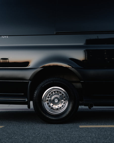 Black luxury RV rental side view with chrome wheel, Mercedes logo, and warm reflections. "TOYS" visible.