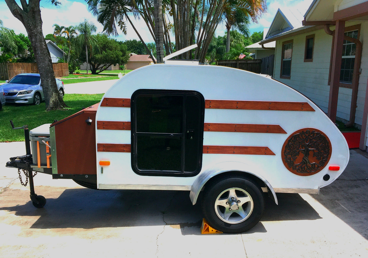 Side view of a unique white teardrop camper with wood trim & Tree of Life art. Great for an RV rental adventure!