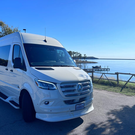 White Mercedes Sprinter van RV rental beside a beautiful lake with a dock under a bright blue sky.