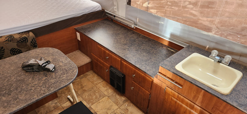 RV rental interior: bed, dining area with gloves, and kitchenette with sink & counter. — photo 7