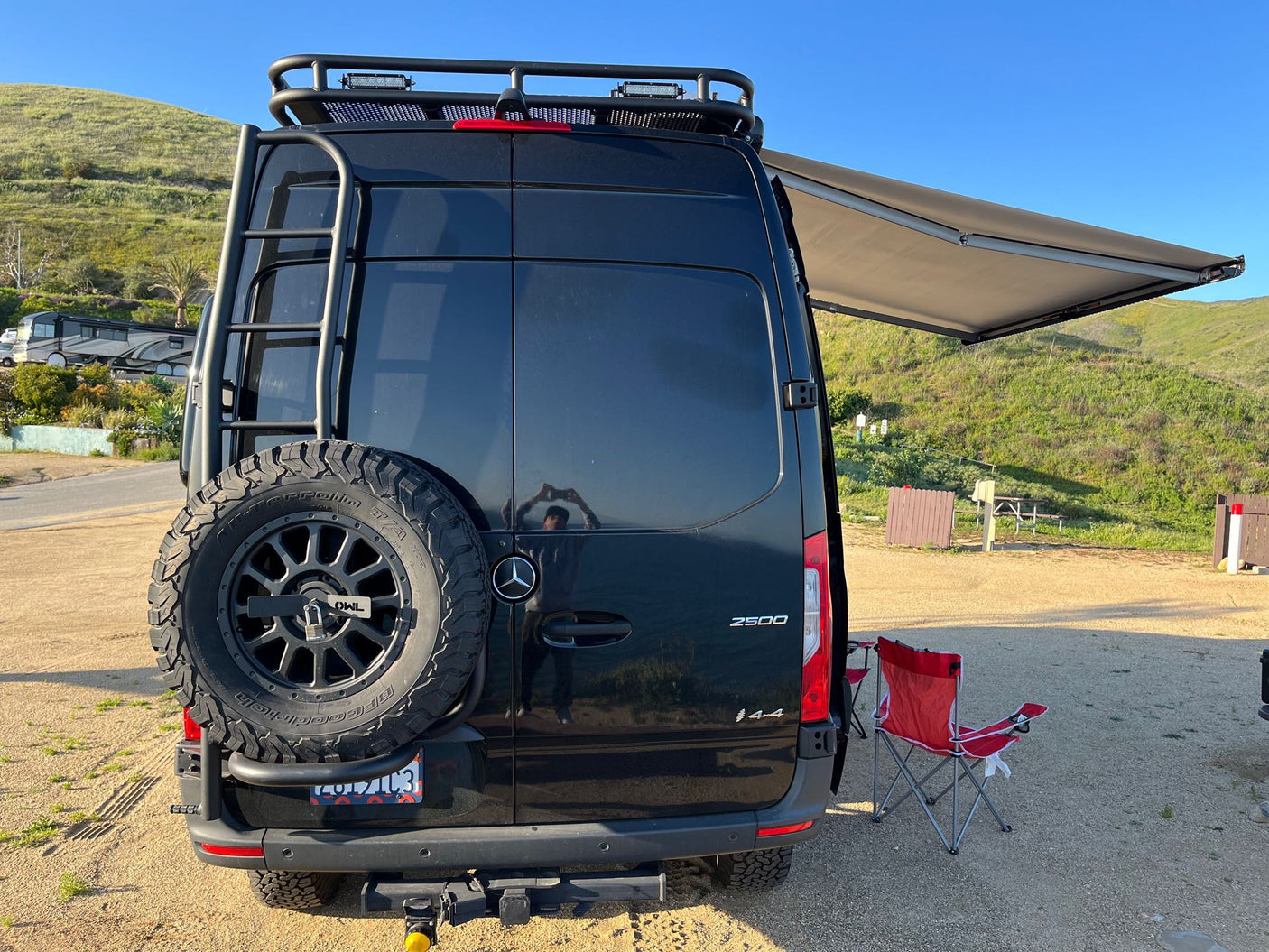 Black Sprinter van, ideal for an RV rental adventure, parked at a scenic outdoor camping spot with its awning extended.