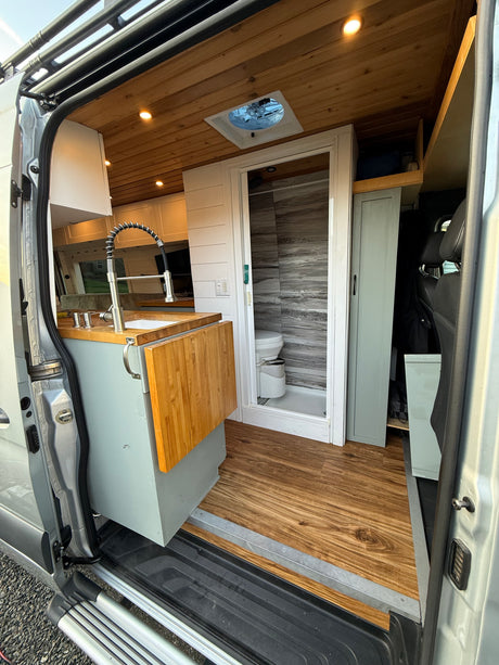 Explore this well-equipped rv rental! View from the open door shows a compact kitchen, shower with toilet, and stylish wood interior.