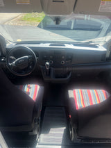 Front cabin of an rv rental van with Ford dashboard, steering wheel, gear shifter, and vibrant patterned seat covers.
