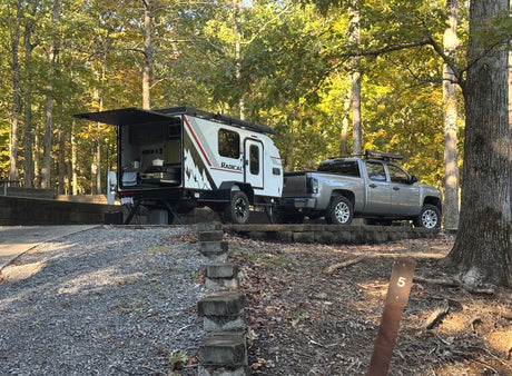 RV rental: Teardrop camper with an outdoor kitchen hitched to a pickup truck, parked at a scenic, wooded campsite.