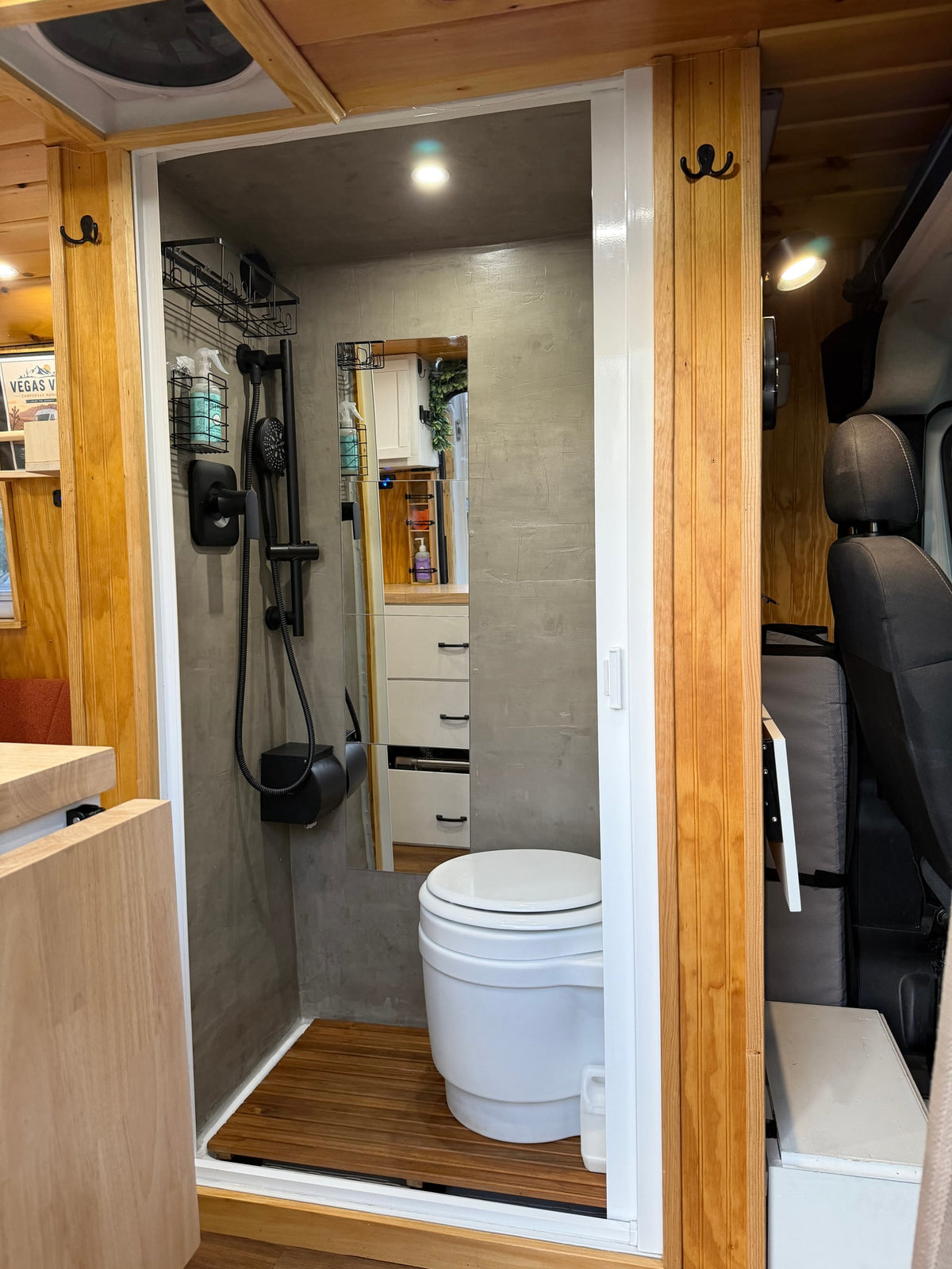 RV rental compact bathroom featuring a shower, composting toilet, and wooden floor. Modern and efficient campervan design. — photo 17