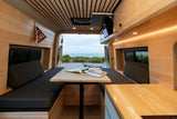 This modern RV rental features a wood-paneled interior, seating, dining table, and a scenic ocean view from the rear.