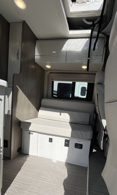 Modern RV rental interior showing a living area with a versatile bench seat, overhead cabinets, and a large window.