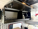 This RV rental overhead cabinet features secure latches, black dishes, storage, controls, and a cozy bed with a chevron accent wall.