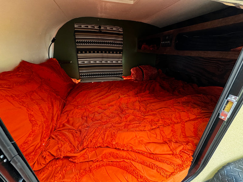 RV rental: Step into a cozy camper bedroom featuring vibrant orange bedding, a southwestern tapestry, and built-in storage. — photo 3