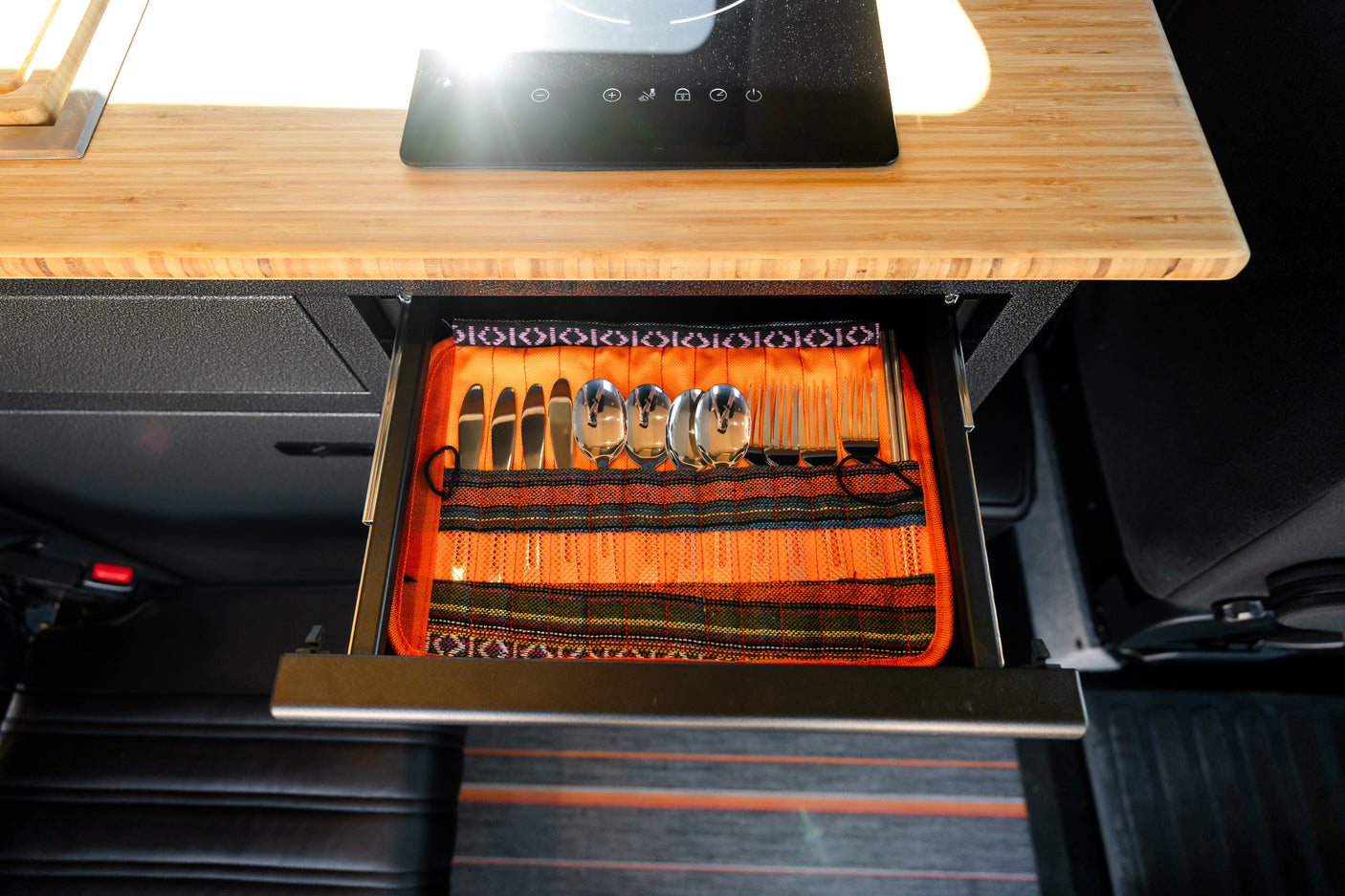 RV rental kitchen drawer with organized cutlery: knives, spoons, forks. Above, bamboo counter with induction cooktop.