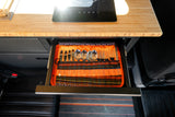 RV rental kitchen drawer with organized cutlery: knives, spoons, forks. Above, bamboo counter with induction cooktop.