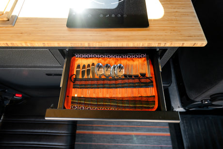 RV rental kitchen drawer with organized cutlery: knives, spoons, forks. Above, bamboo counter with induction cooktop.