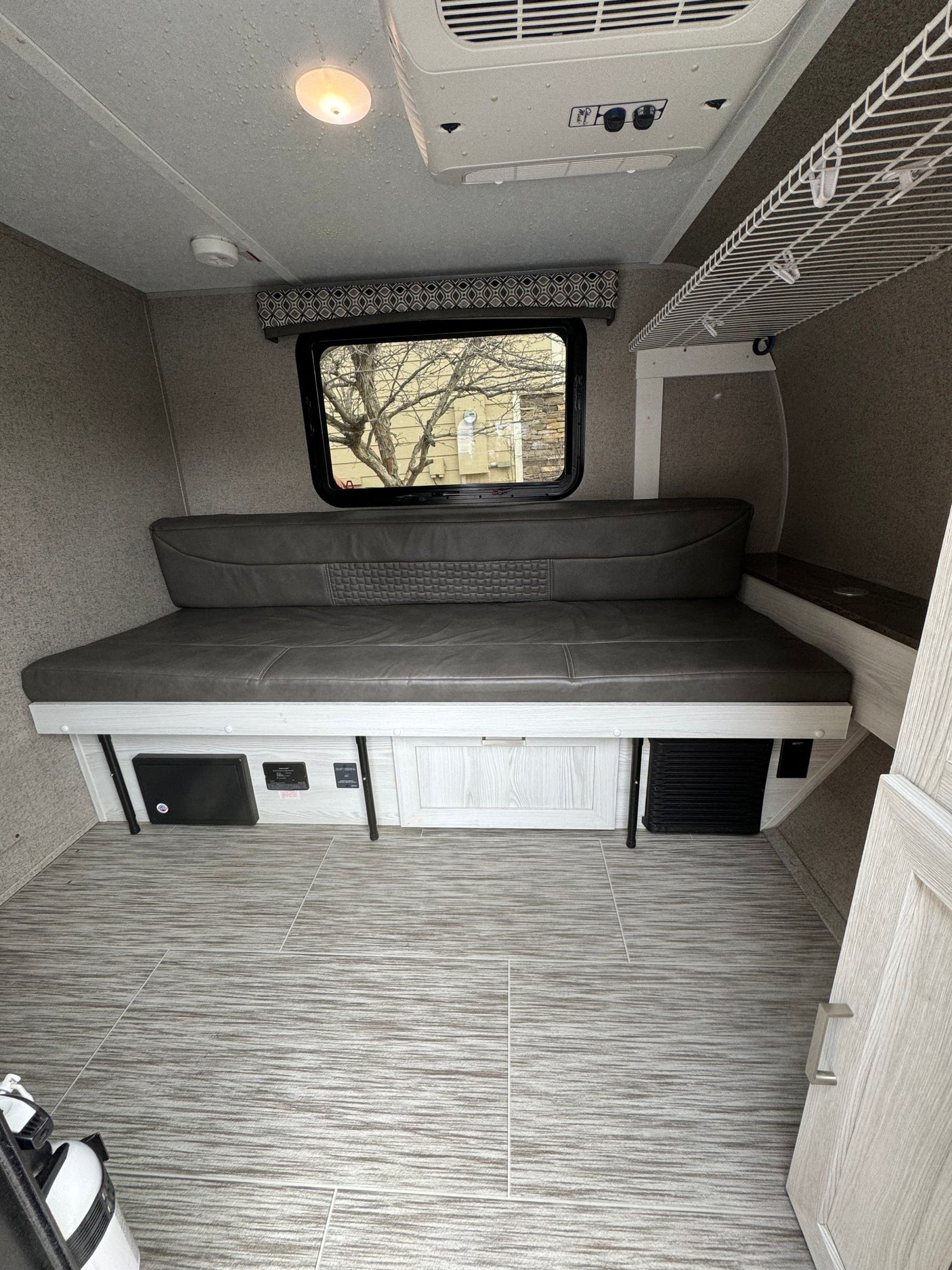 Cozy RV rental interior with a gray sofa bed, large window, ceiling AC unit, and light wood-tone flooring and cabinetry.