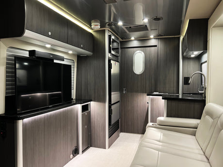 Step into this modern RV rental's interior, featuring a living area with TV, kitchen, and comfortable lounge seating.