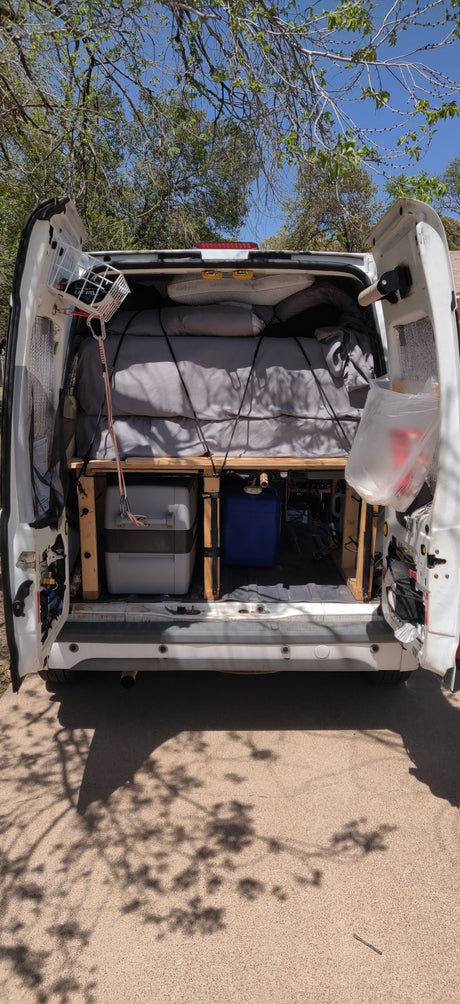 White RV rental camper van's rear open, showcasing a comfy bed & under-bed storage for road trips.