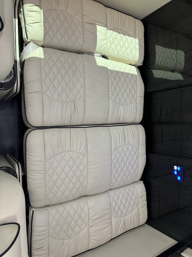 Cream quilted sleeping area in an RV rental. Four stacked cushions with dark piping line the interior wall. — photo 13