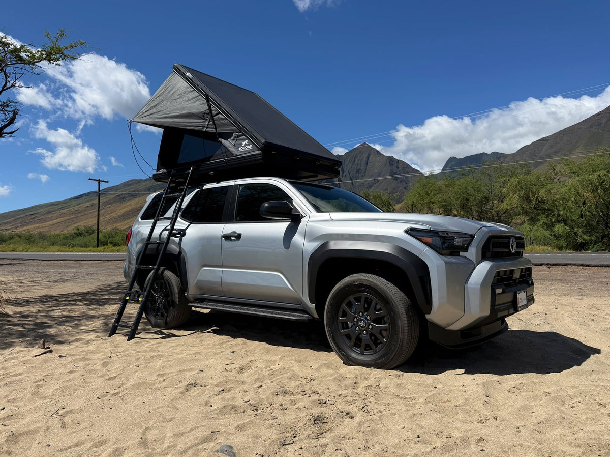 Adventure-ready RV rental! This silver SUV with a deployed rooftop tent is parked on sand