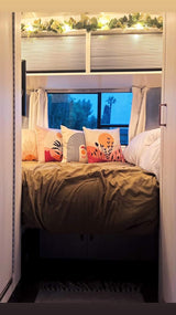 Cozy RV rental bedroom with comfy bed, artistic pillows, warm lights, and a serene night view for travel.