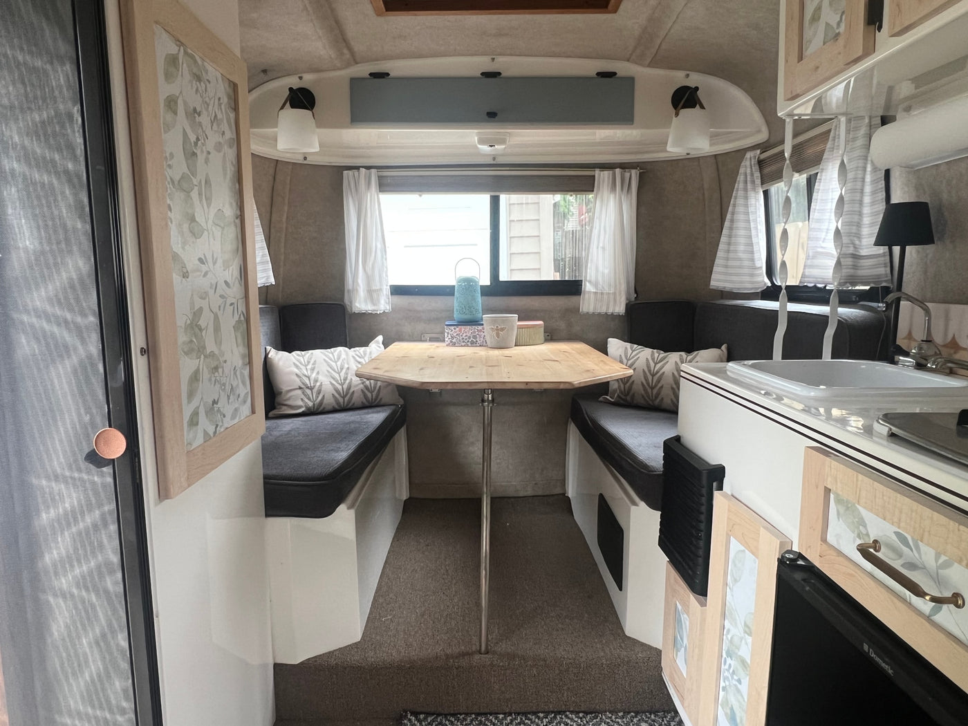 Explore this cozy RV rental interior featuring a renovated dining area, stylish leaf decor, and compact kitchen space. — photo 2