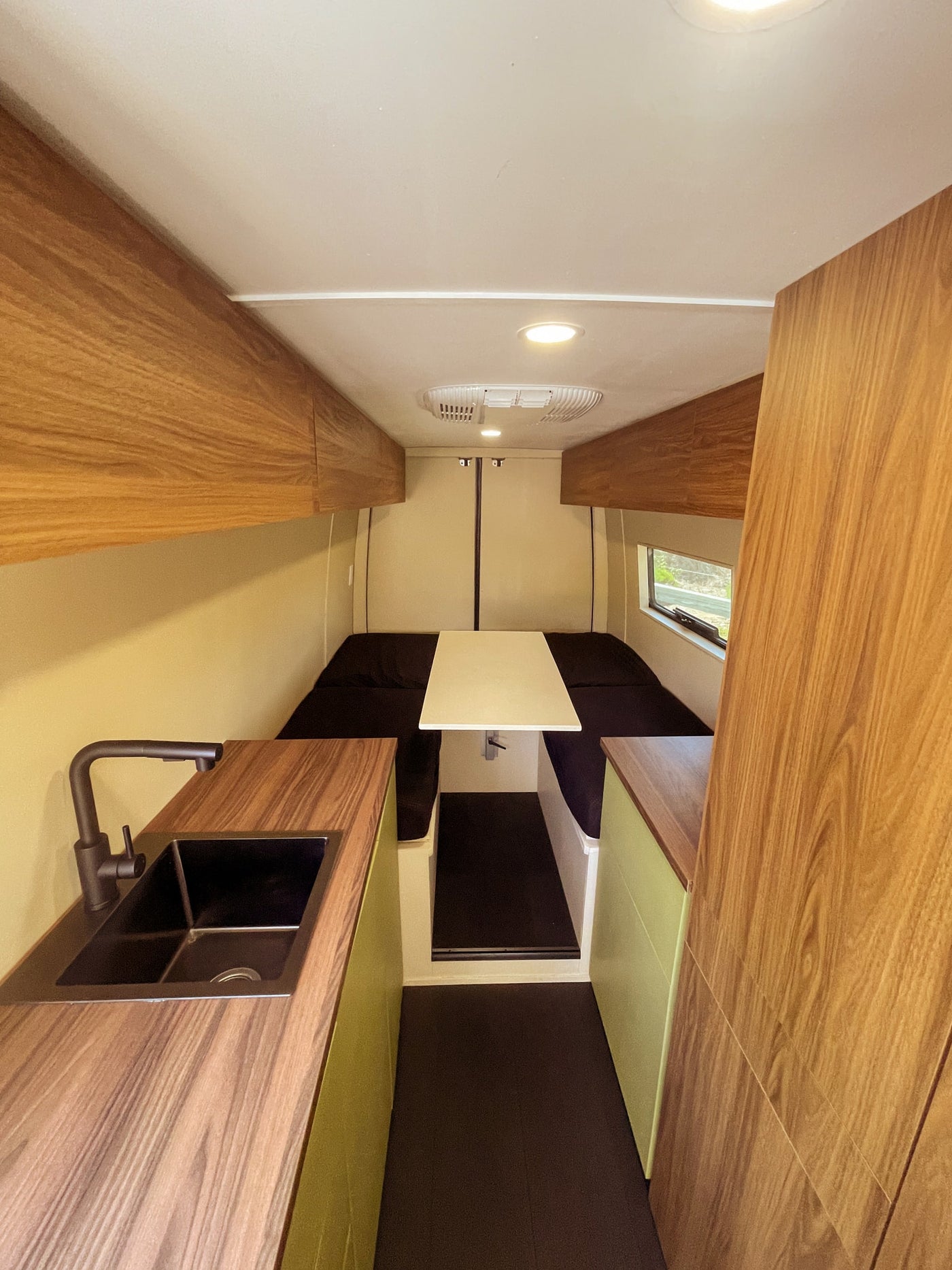 Bright RV rental interior: Modern camper van with wooden cabinets, sink, dining table, and seating area. — photo 11