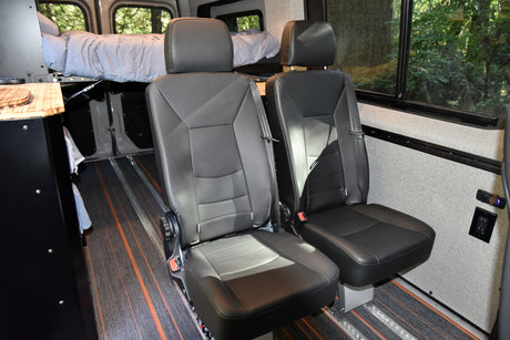 Inside this RV rental: two black passenger seats and an elevated bed, providing flexible seating & sleeping in a camper van.