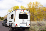 A white Geo Pro RV rental, towed by a Jeep, parked on a road. Ready for scenic road trips and outdoor adventures.