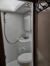 RV rental bathroom: A compact space with white fixtures including a toilet, sink with shower hose, and mirror. Overhead storage visible.