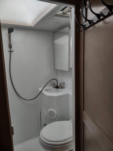 RV rental bathroom: A compact space with white fixtures including a toilet, sink with shower hose, and mirror. Overhead storage visible.