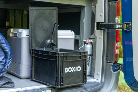 This rv rental features a practical Boxio portable sink, cooler, and fire extinguisher setup inside a camper van for convenience.