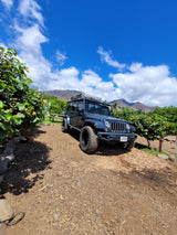 Adventure-ready Jeep Wrangler RV rental with rooftop tent against Hawaiian mountains & blue sky. Perfect for outdoor travel!