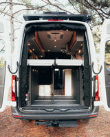 An rv rental camper van's open rear reveals a smart interior with raised bed, lower storage, and ceiling AC unit.