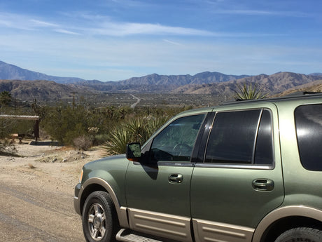 Green SUV parked on a dirt road, offering scenic desert views and distant mountains. Perfect for an RV rental adventure.