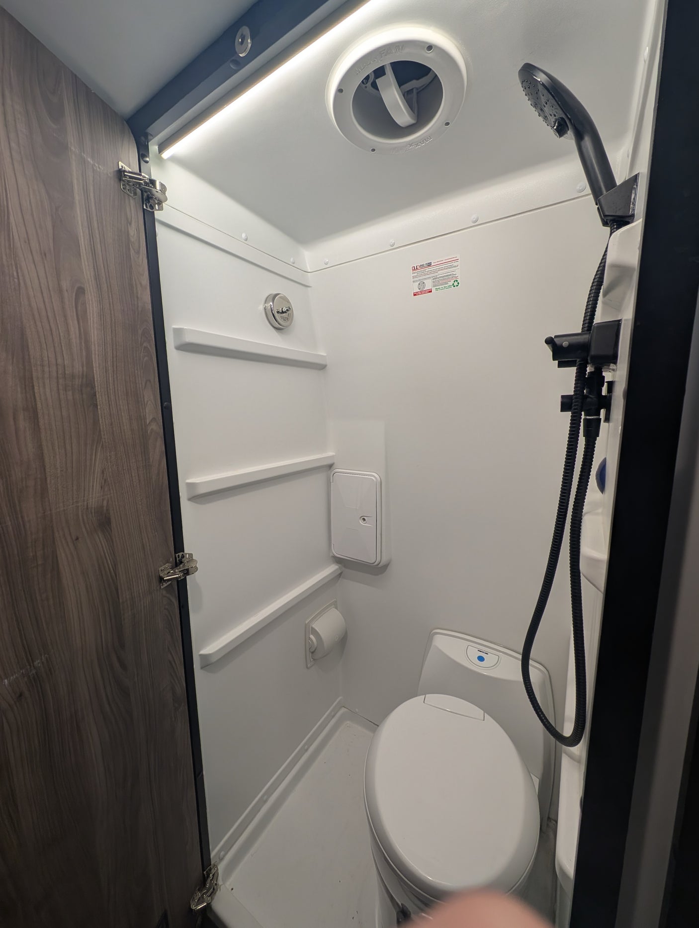 This rv rental features a compact bathroom with a white toilet, handheld shower, and ceiling vent fan for comfort.