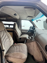 Detailed RV rental interior: beige seats, dashboard, and a view into the rear camper area with a sink.