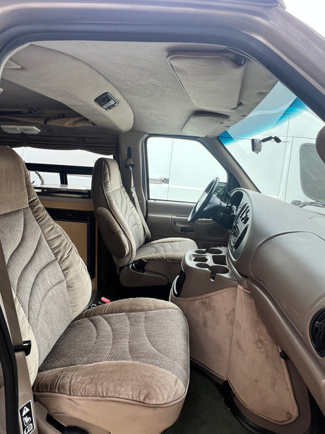 Detailed RV rental interior: beige seats, dashboard, and a view into the rear camper area with a sink.