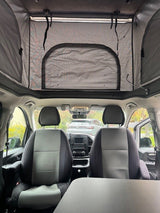 Inside an rv rental: Looking forward past front seats to the dashboard, with a spacious pop-top tent extended above.