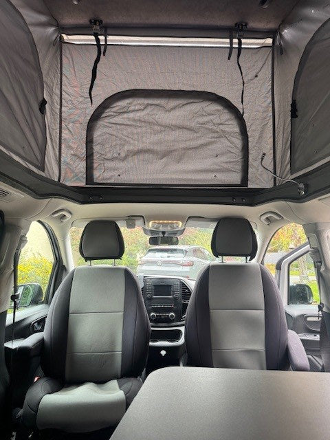 Inside an rv rental: Looking forward past front seats to the dashboard, with a spacious pop-top tent extended above. — photo 4