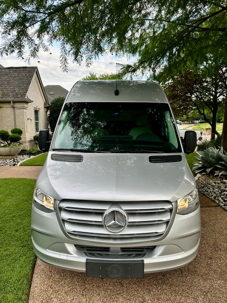 Front view of a silver Mercedes-Benz Sprinter van, ideal for an RV rental. Parked outside a home.